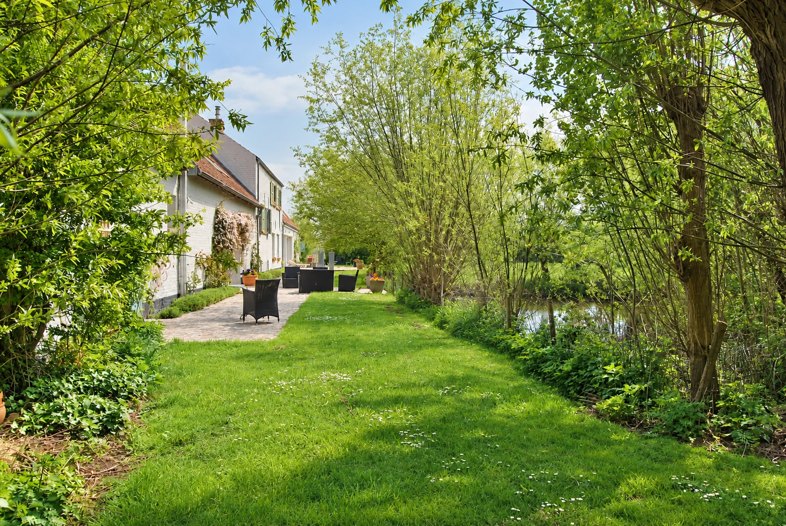 Het witte huis links, het terras en de vijver rechts tussen de wilgen